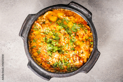 Delicious Brazilian fish moqueca with tomato, onion, olive oil, coriander and orocum seed. Made in clay pot on white table and black background.