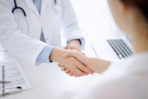 Doctor and patient shaking hands while sitting opposite of each other at the table in clinic, just hands close up. Medicine concept