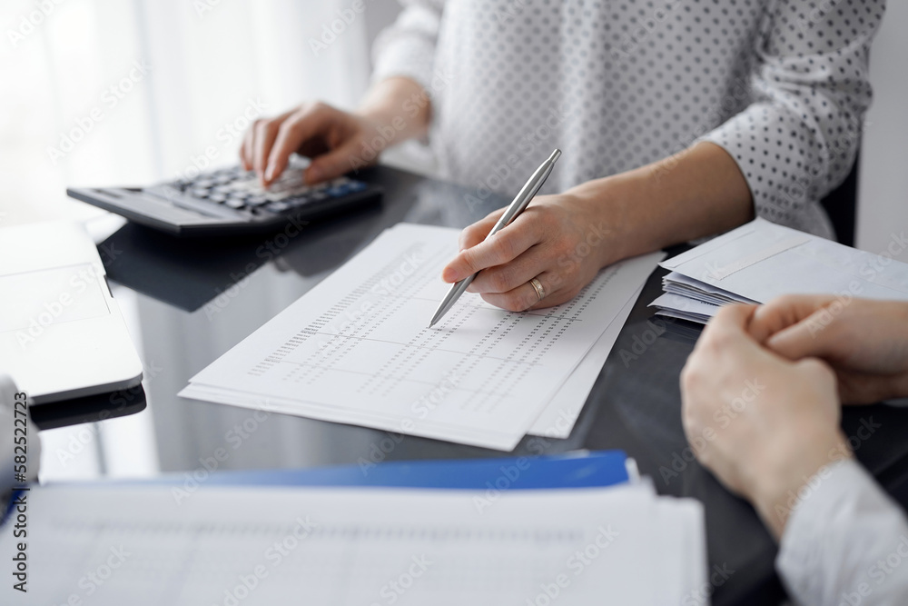 Woman accountant using a calculator and laptop computer while counting taxes for a client. Business audit and finance concepts