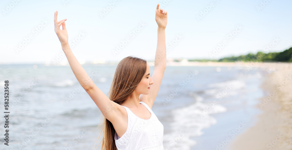 Happy smiling woman in free happiness bliss on ocean beach standing with raising hands. Portrait of a multicultural female model in white summer dress enjoying nature during travel holidays vacation Happy smiling woman in free happiness bliss on ocean beach standing with raising hands. Portrait of a multicultural female model in white summer dress enjoying nature during travel holidays vacation