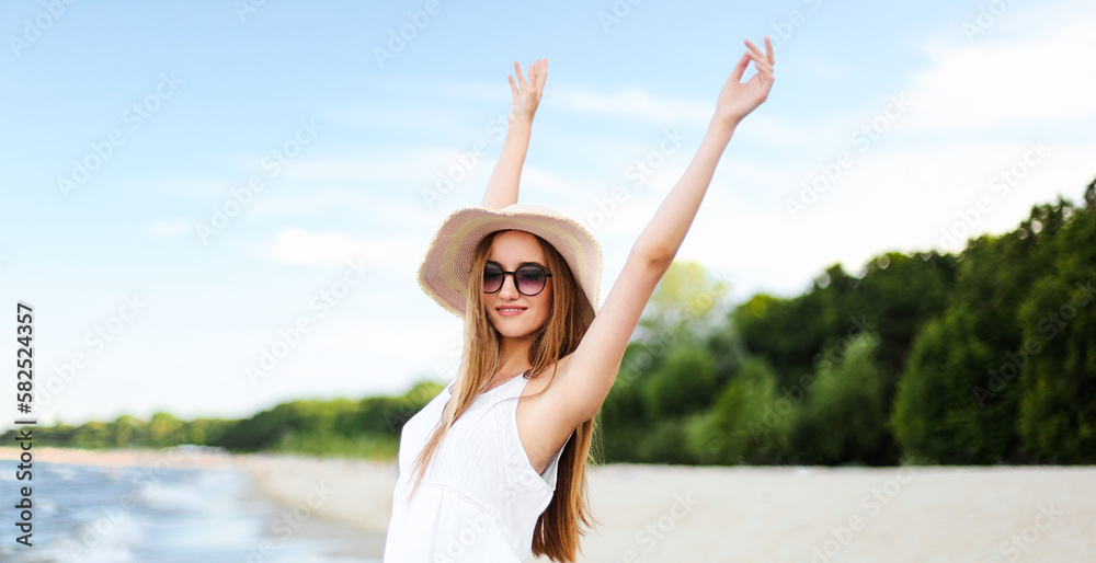 Happy smiling woman in free happiness bliss on ocean beach standing with a hat, sunglasses, and rasing hands. Portrait of a multicultural female model in white summer dress enjoying nature. Happy smiling woman in free happiness bliss on ocean beach standing with a hat, sunglasses, and rasing hands. Portrait of a multicultural female model in white summer dress enjoying nature.
