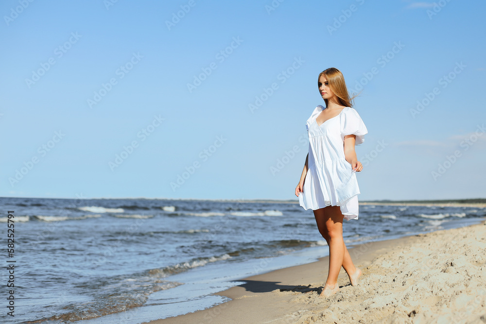 Happy smiling beautiful woman is walking on the ocean beach in a white summer dress Happy smiling beautiful woman is walking on the ocean beach in a white summer dress