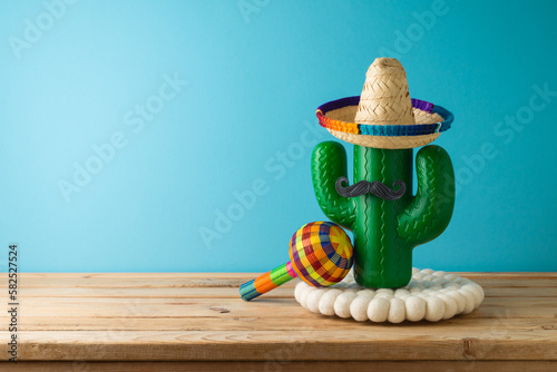 Mexican holiday wooden table with cactus, party sombrero hat and maracas over blue background