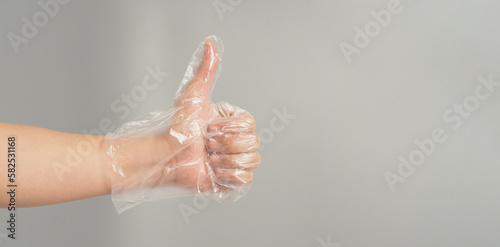 Left hand is wearing a disposable plastic glove and do like hand sign on grey background.