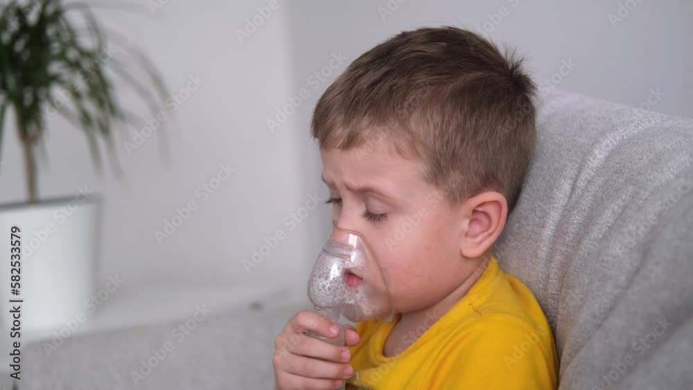 Little boy makes an inhalation vapor . Child is sick bronchitis and breathes through an inhaler in home. Side view Little boy makes an inhalation vapor . Child is sick bronchitis and breathes through an inhaler in home. Side view