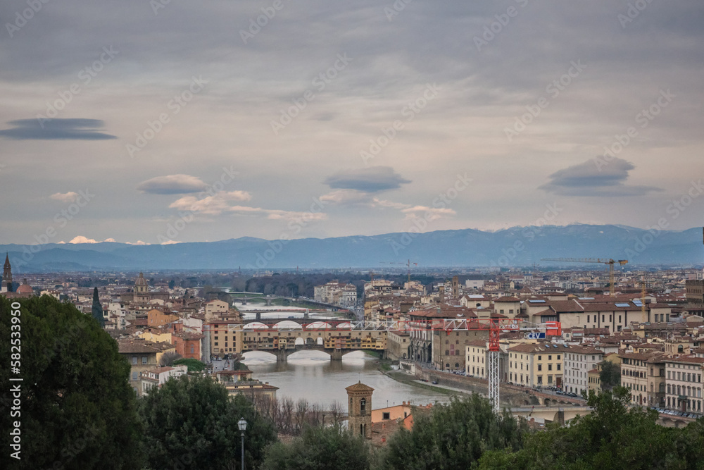 Florence cityscape in a cloudy day with ponte vecchio and snowy mountains in background
