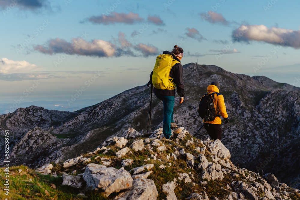 group of two mountaineers with backpack and trekking poles hiking up a mountain peak. sport, adventure and outdoor activity. weekend activities.