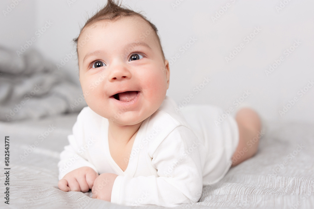 The baby lies on his stomach on the bed. A beautiful baby smiles. Mockup for advertising, design, celebration, postcards.