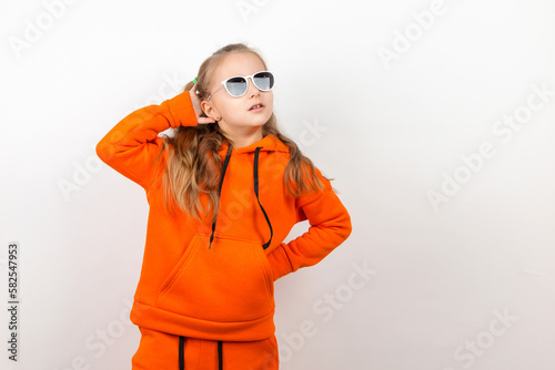 A little girl in an orange hoody and sunglasses, emotions of joy and a sunny day, portrait. On a white background. © Plutmaverick