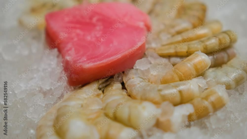 The tuna steak lies on the beautifully laid tails of a large shrimp. The tuna steak and shrimp tails lie on pieces of ice. Close-up. Slow motion. The tuna steak lies on the beautifully laid tails of a large shrimp. The tuna steak and shrimp tails lie on pieces of ice. Close-up. Slow motion.