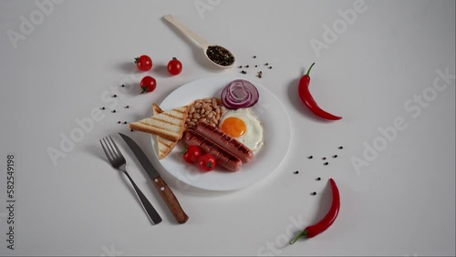 Traditional English Breakfast. Plate with Fried egg, two fried sausages, grilled bread toast, canned beans, blue onions and cherry tomatoes on a White Background. Copy space