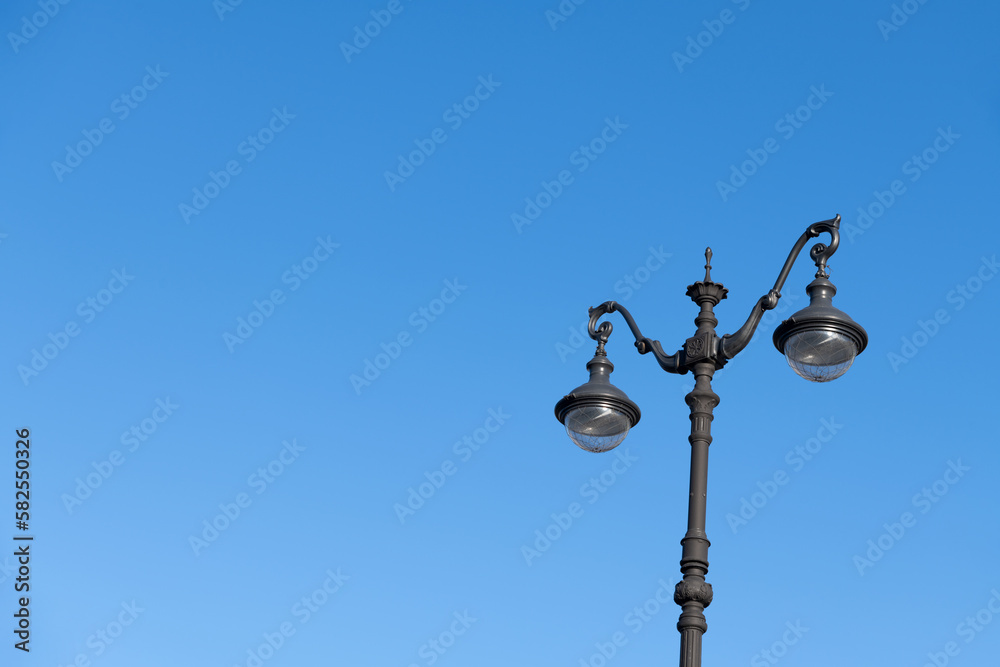 Close-up view of black ornate street lamppost with led lamps standing against clear blue sky in the morning. Copy space for your text. Soft focus. City life theme. Close-up view of black ornate street lamppost with led lamps standing against clear blue sky in the morning. Copy space for your text. Soft focus. City life theme.