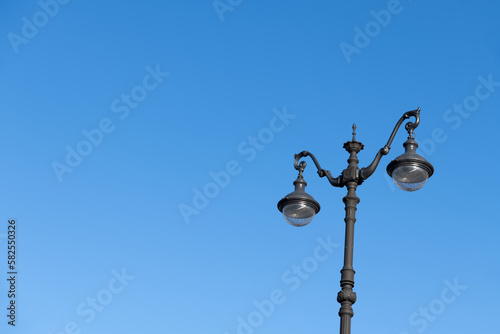 Close-up view of black ornate street lamppost with led lamps standing against clear blue sky in the morning. Copy space for your text. Soft focus. City life theme.