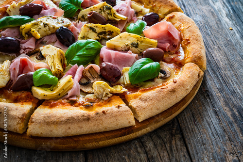 Pizza capricciosa with cooked ham, mozzarella, artichoke   and vegetables on wooden table
 photo