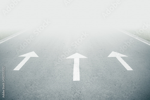 Three white arrow sign on road goes into fog. Direction way sign. Moving forward concept. Unclear ahead or negative tomorrow concept. Empty copy space.