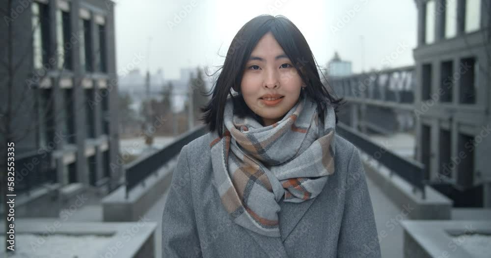 A young beautiful Asian woman stands between business buildings and smiles joyfully. Beautiful people. Portrait of attractive girl. Spring. A young beautiful Asian woman stands between business buildings and smiles joyfully. Beautiful people. Portrait of attractive girl. Spring.
