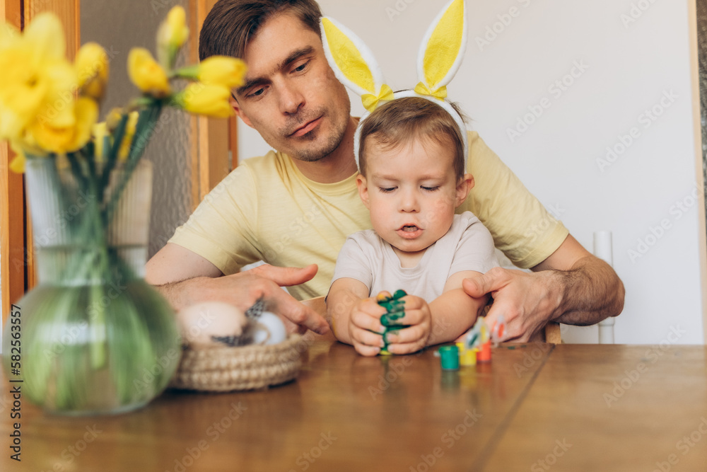 Fototapeta premium dad and child in bunny ear headbands decorating eggs for Easter