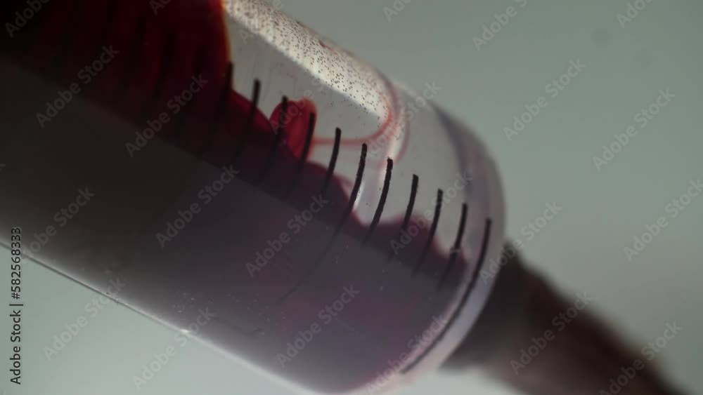Extreme close-up drawing in blood into syringe. Macro shot medical procedure syringe pulling red liquid into saline solution isolated on gray background Extreme close-up drawing in blood into syringe. Macro shot medical procedure syringe pulling red liquid into saline solution isolated on gray background