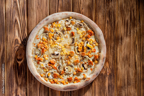 Appetizing pizza on a creamy sauce with mushrooms, corn, chicken fillet and mozzarella cheese on woden background