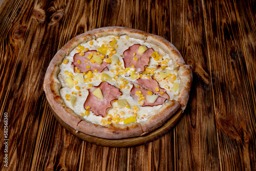 Delicious pizza with ham, pineapple, corn on a creamy base on woden background. Hawaiian pizza photo