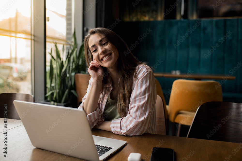 Woman smiling while working from her laptop in a restaurant. Woman smiling while working from her laptop in a restaurant.