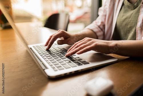 Close up of a woman typing on a laptop keyboard while sitting in a restaurant 