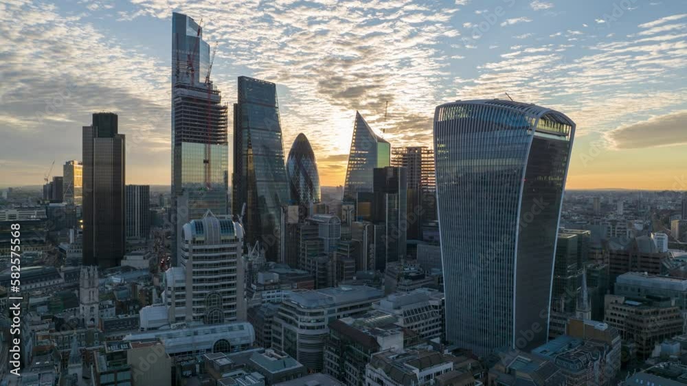 Walkie Talkie, Gherkin and other famous modern design skyscrapers against rising sun. Aerial hyperlapse shot of clouds moving in sky. London, UK