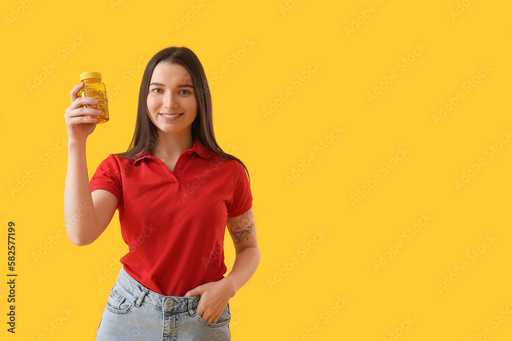 Young woman with bottle of vitamin supplements on yellow background