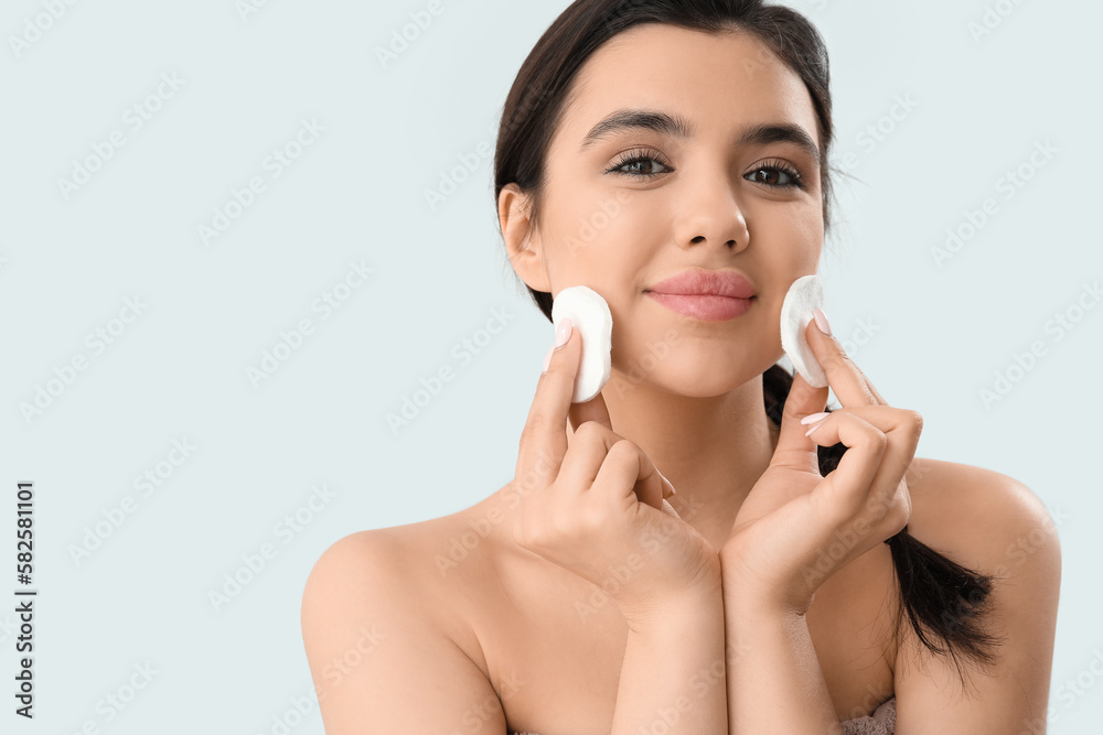 Young woman removing makeup with cotton pads on light background Young woman removing makeup with cotton pads on light background