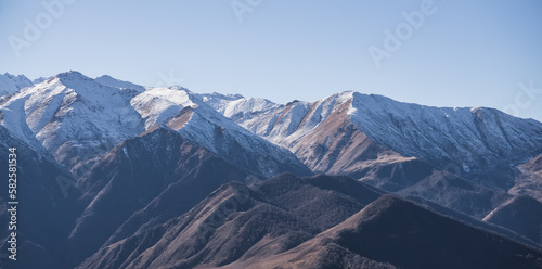 Mountain panorama of the ridge in the autumn mountains with yellowed grass and forest and the first snow on the tops of the mountains, autumn mountain panorama