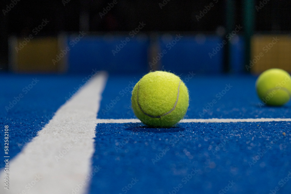 Selective focus, two balls and the line of a blue paddle tennis court.