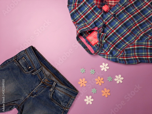 Spring look. Copy space. Top view. Street fashion for girls and women in country style. Jeans and plaid shirt lie on pink background with decorative flowers. Flat lay. Place for text.