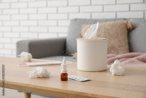 Nasal drops with pills and tissue box on table in living room, closeup. Allergy concept