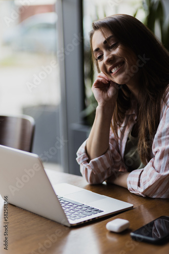 A young woman smiling at a coffee shop while working on her laptop.