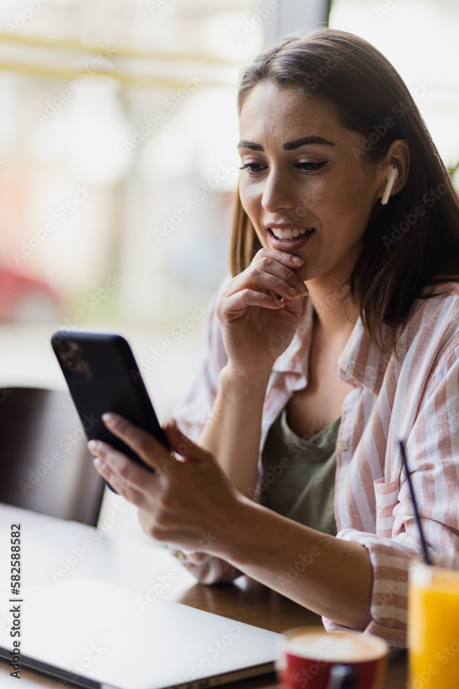Portrait of a stylish woman in a restaurant wearing wireless headphones and browsing her phone. Portrait of a stylish woman in a restaurant wearing wireless headphones and browsing her phone.