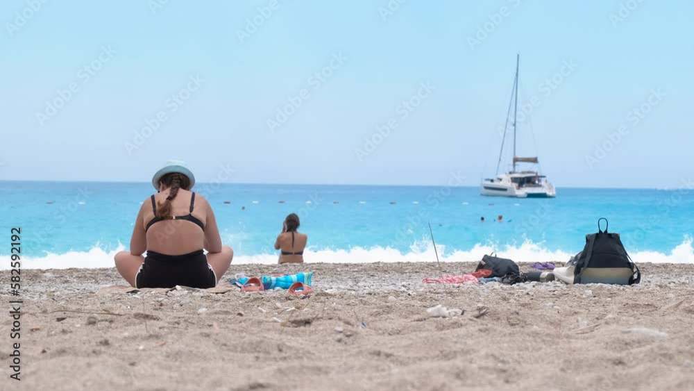 Female travelers with backpack sit on bay. A view of female travelers relax on the beach and enjoy the azure sea under sun in summer. Female travelers with backpack sit on bay. A view of female travelers relax on the beach and enjoy the azure sea under sun in summer.