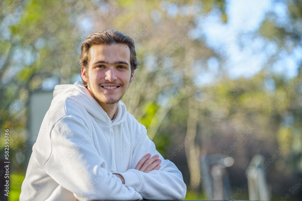 Portrait of a smiling handsome young man at the park in summer. Happy man looks to the camera, outdoor portrait. Smiling face of a male model with brown hair. Guy with a smile looking camera Portrait of a smiling handsome young man at the park in summer. Happy man looks to the camera, outdoor portrait. Smiling face of a male model with brown hair. Guy with a smile looking camera