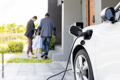 Cuadro en lienzo Focus closeup electric vehicle recharging battery from home electric charging station with blurred family in background