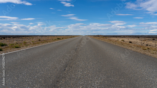 A long straight road without lines that crosses the Atacama desert in Chile. Sun with clouds in the blue sky.