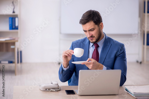 Young male employee drinking coffee in the office