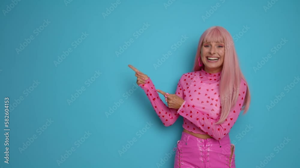 Nice girl in pink clothes standing on blue studio background, points fingers towards copy space on her right and smiles happily showing enjoyment, copy space Nice girl in pink clothes standing on blue studio background, points fingers towards copy space on her right and smiles happily showing enjoyment, copy space