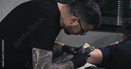 Close up tattoo artist shows the process of getting black tattoos with paint. The master works in black sterile gloves. Master tattoo artist in studio.