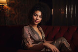 Elegant woman with natural curly hair and a bright smile sitting on a vintage velvet sofa, generative ai