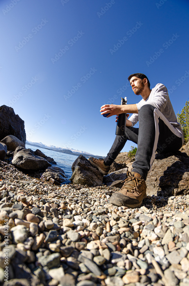 chico mirando el paisaje sentado a la orilla rocosa del lago tomando ...