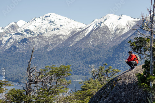 hombre en la cima de un cerro, sobre una roca, observando el paisaje de lagos y montañas nevadas © Beto.dlf