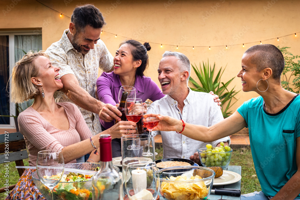 Group of friends celebrating life, toasting with wine, laughing and having fun during barbecue garden dinner party.