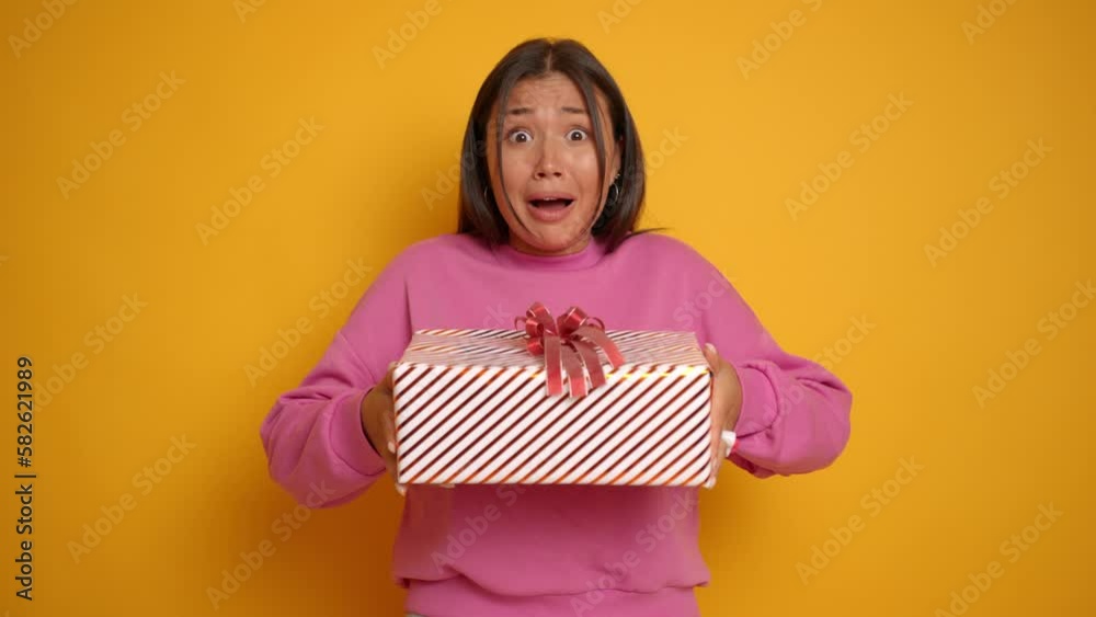 Happy Asian brunette woman get a present gift for her birthday she can't believe in that so she is amazed isolated next to yellow wall