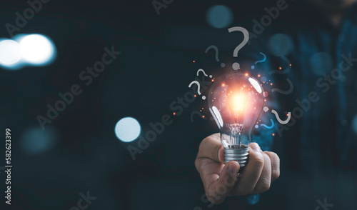 Businessman holding glowing lightbulb and question mark with copy space for creative thinking idea and problem solving concep