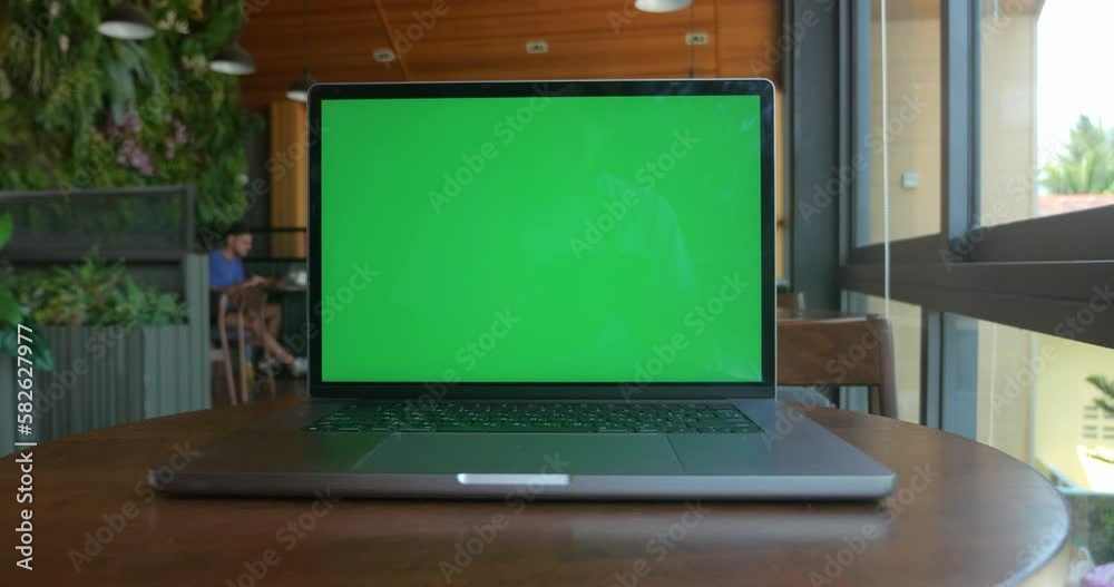 Laptop computer with green screen chroma key on table at cozy cafe near