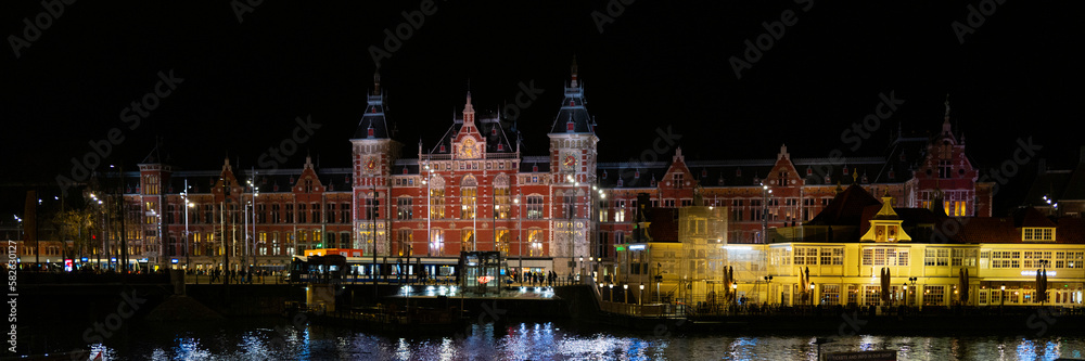 Amsterdam Centraal buildings, water reflections, and busy street at night in Netherlands, vibrant long exposure photography